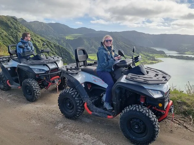 Two people on ATVs parked on a dirt road with lake views.