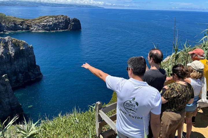 Ein Reiseleiter deutet für eine Touristengruppe in Richtung Ozean.