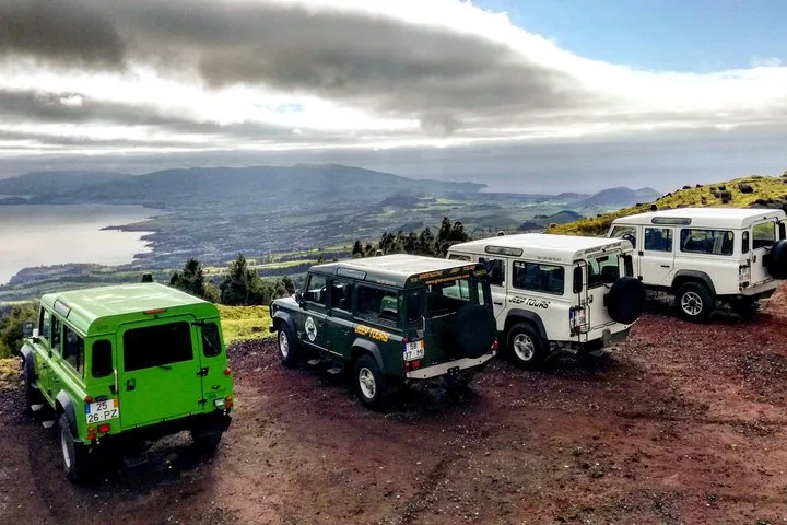 Vier bunte Jeeps, geparkt auf einem Erdhügel mit Seeblick.