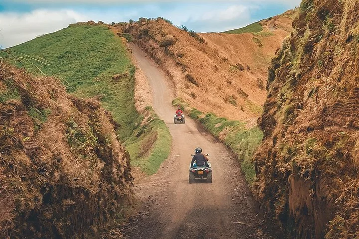 Zwei ATVs fahren einen steilen, schmalen Schotterweg zwischen Hügeln hinunter.